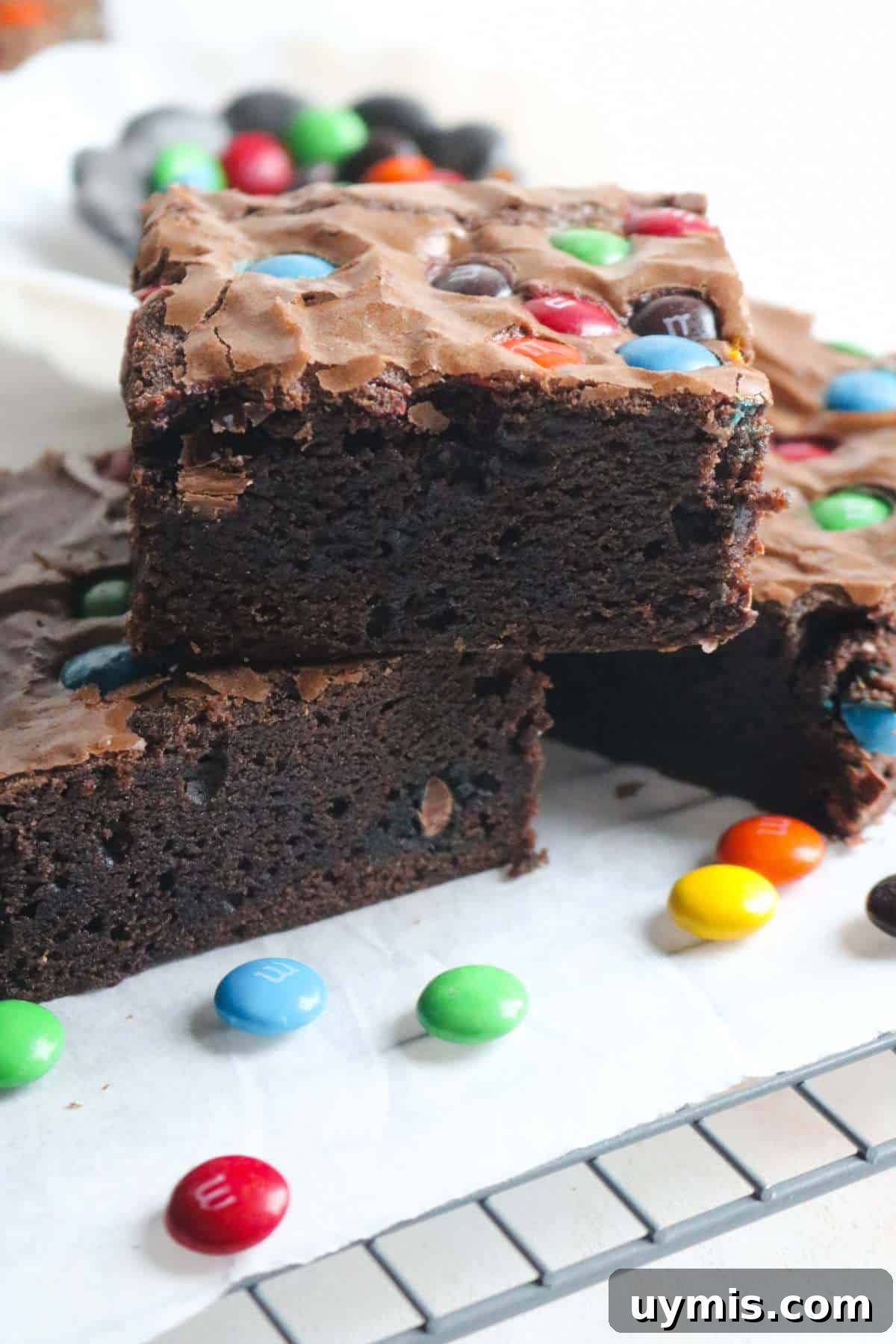 Thick and Chewy M&M Brownies Recipe 2 stack of three thick and fudgy m&m brownies with lots of candies sprinkled around them.