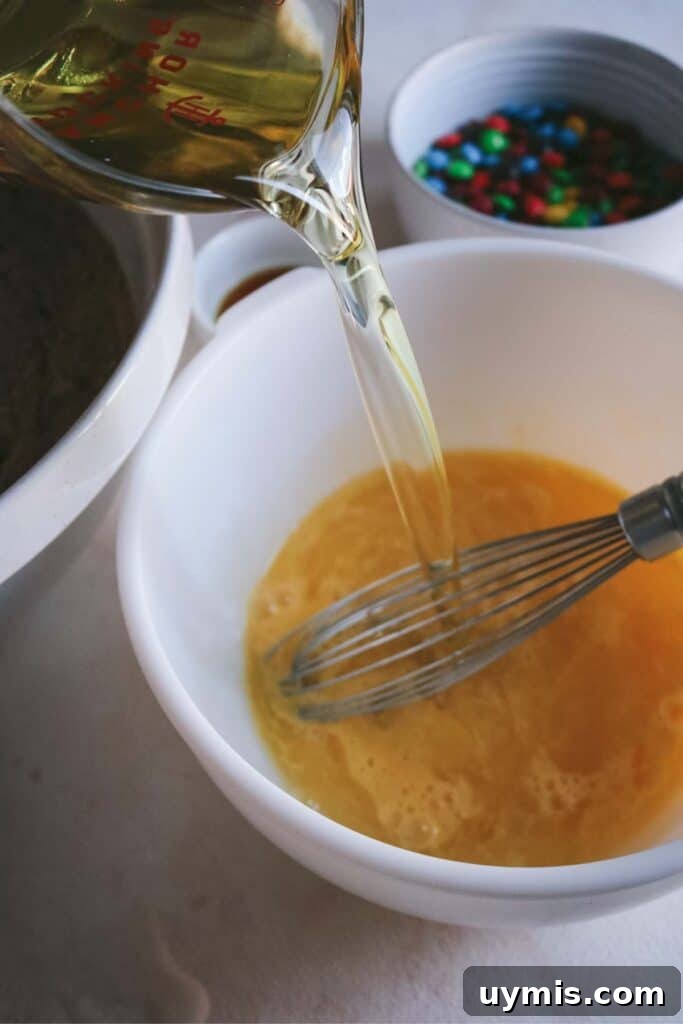 Thick and Chewy M&M Brownies Recipe 15 adding vegetable oil to whisked eggs for moist m&m brownies.