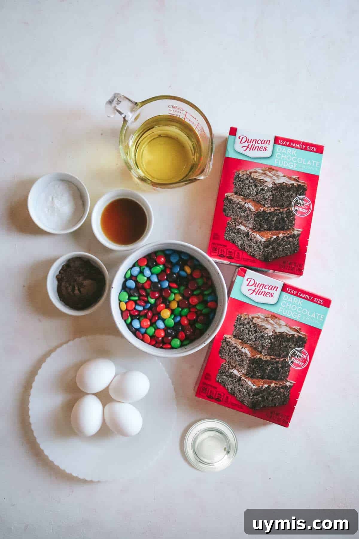 Thick and Chewy M&M Brownies Recipe 4 overhead view of all the ingredients to make fudgy m&m brownies including water, oil, brownie mix, eggs, and more.