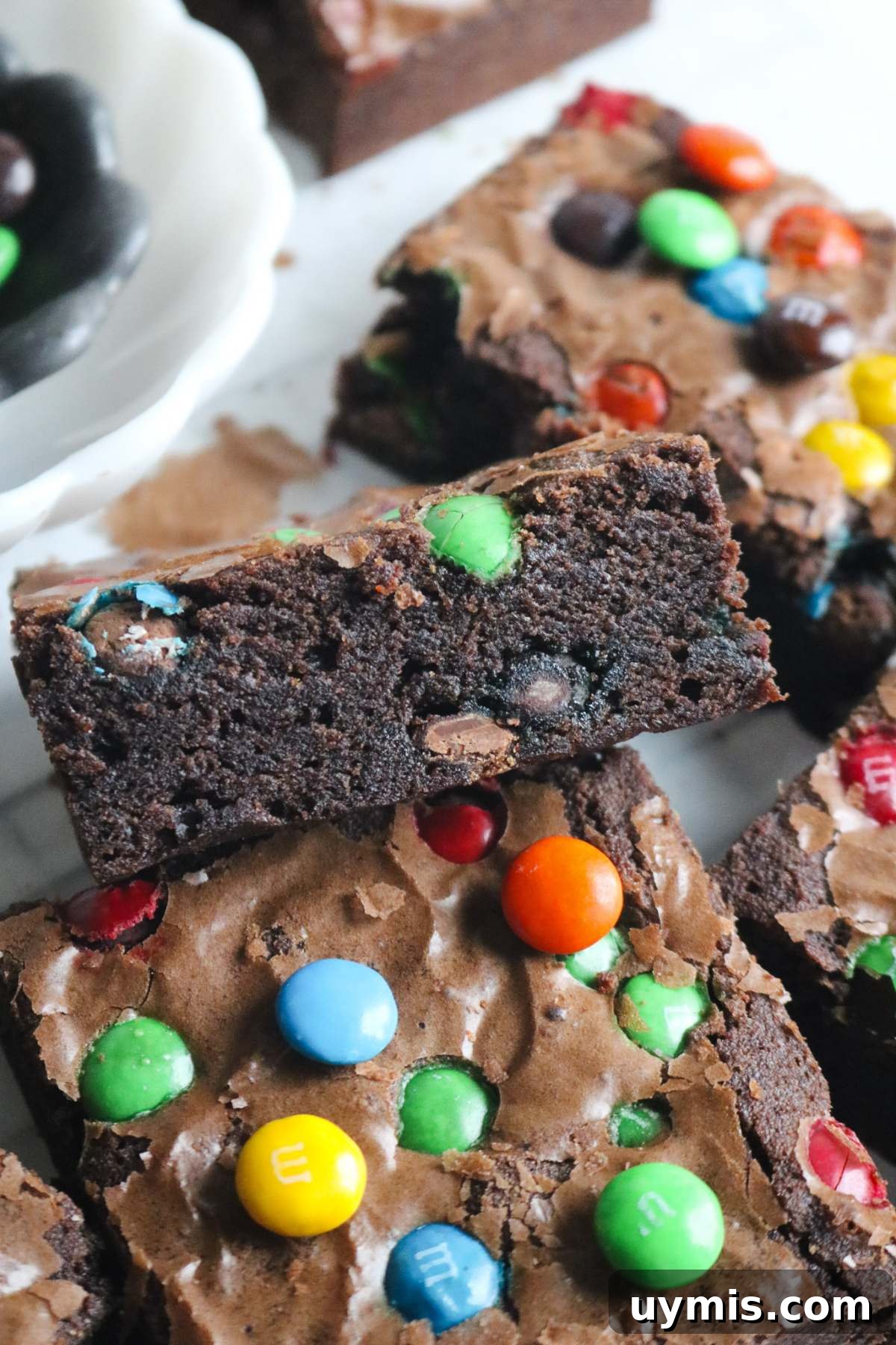 Thick and Chewy M&M Brownies Recipe 6 side view of a sliced m&m brownie with lots candies inside and sprinkled over top.