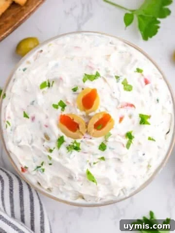 A small bowl of olive dip topped with sliced olives and garnished with parsley.