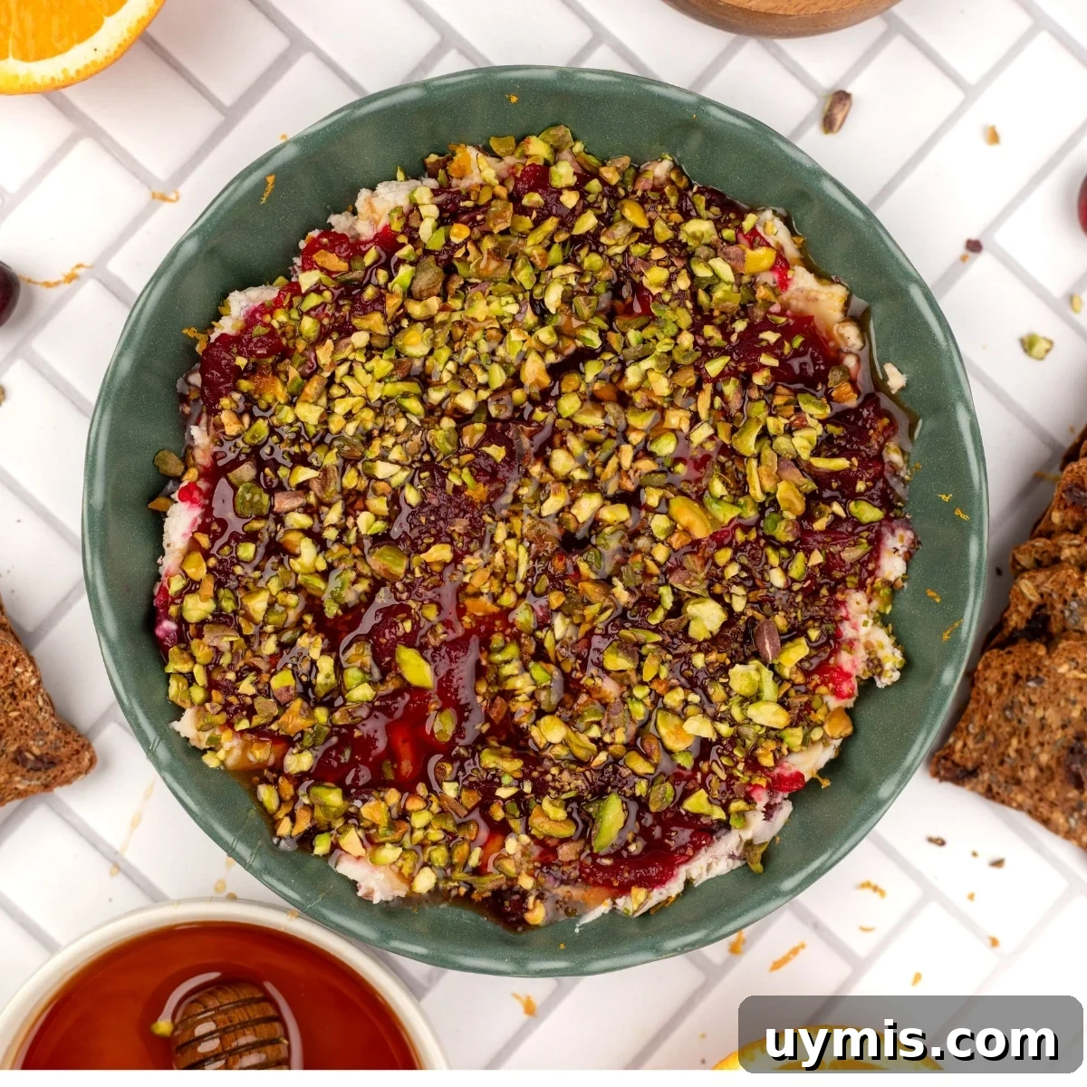 A bowl of boursin dip with cranberry sauce and pistachios.