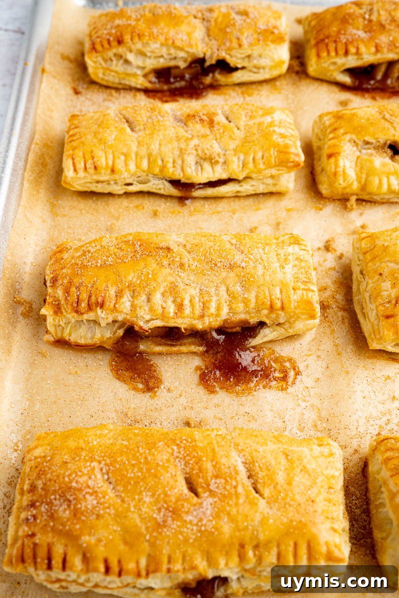 Warm Apple Hand Pies with Cinnamon and Flaky Crust 6 Baked apple hand pies on a baking sheet after coming out of the oven.
