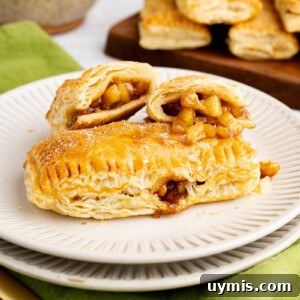 An apple hand pie split into two pieces sits next to a whole apple hand pie on a plate for serving.