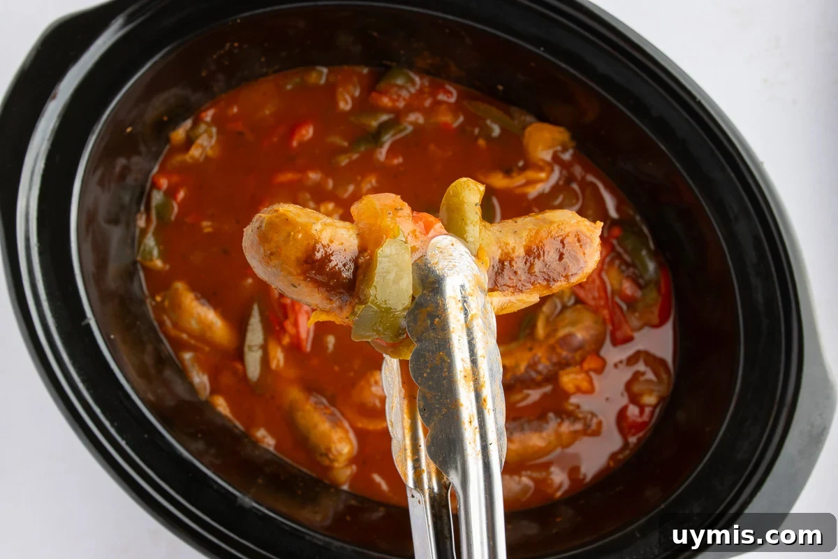 Crockpot Sausage and Peppers Recipe 12 Sausage and peppers held in tongs over top of crockpot.