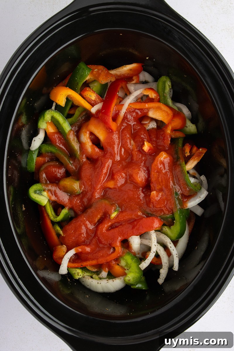 Crockpot Sausage and Peppers Recipe 7 Tomato sauce is poured over peppers and onions in slow cooker.