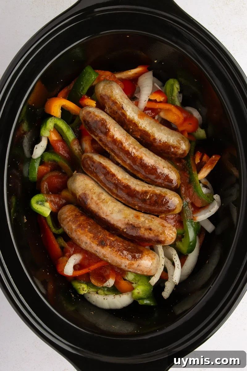 Crockpot Sausage and Peppers Recipe 9 Browned sausages are placed over pepper, onions and tomato sauce mixture in slow cooker.