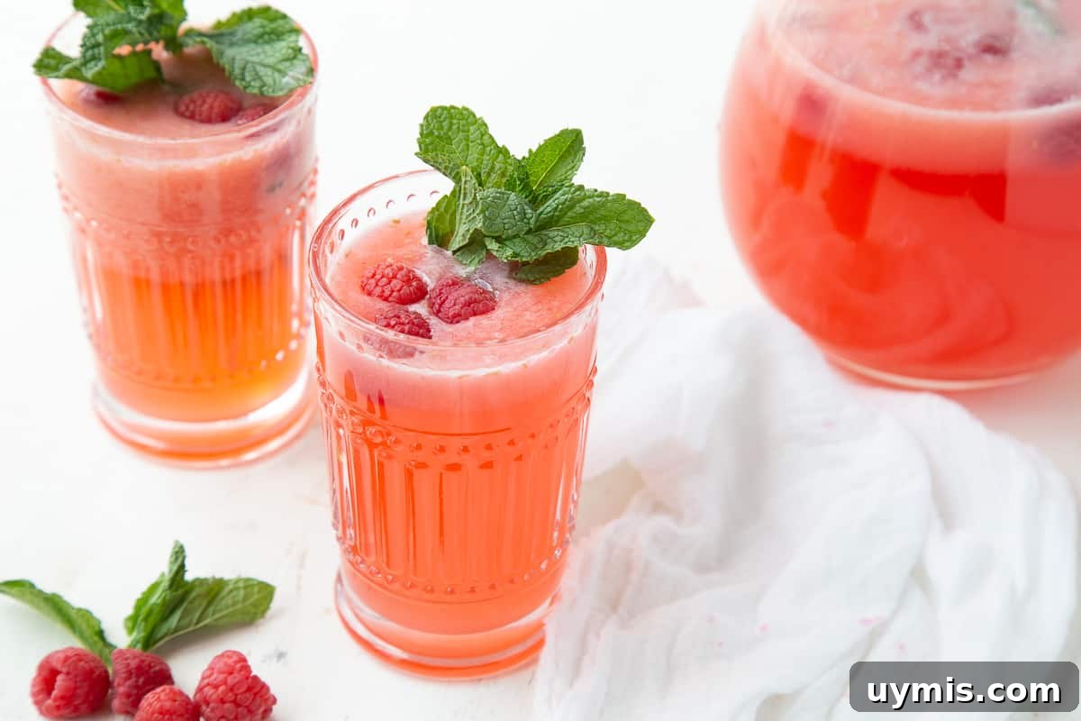 Two Ingredient Raspberry Lemonade Recipe 7 glasses of raspberry lemonade next to a glass pitcher.