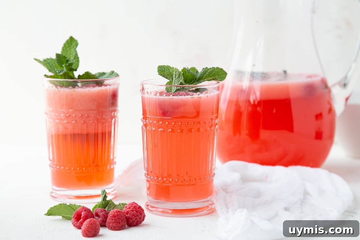 Two Ingredient Raspberry Lemonade Recipe 8 glasses of raspberry lemonade next to a pitcher and fresh raspberries.