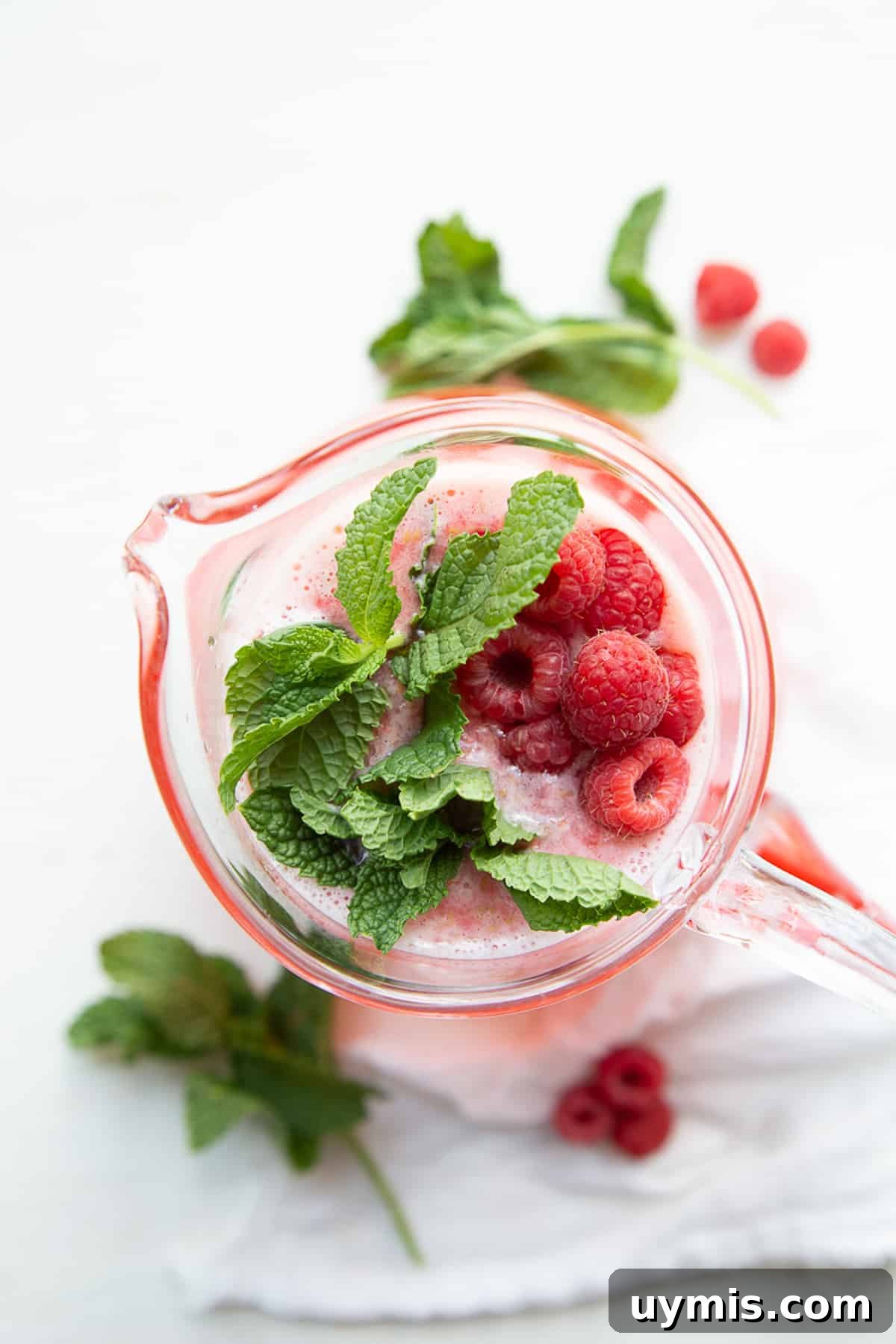 Two Ingredient Raspberry Lemonade Recipe 9 top-down view of a pitcher of raspberry lemonade garnished with fresh raspberries and mint leaves.