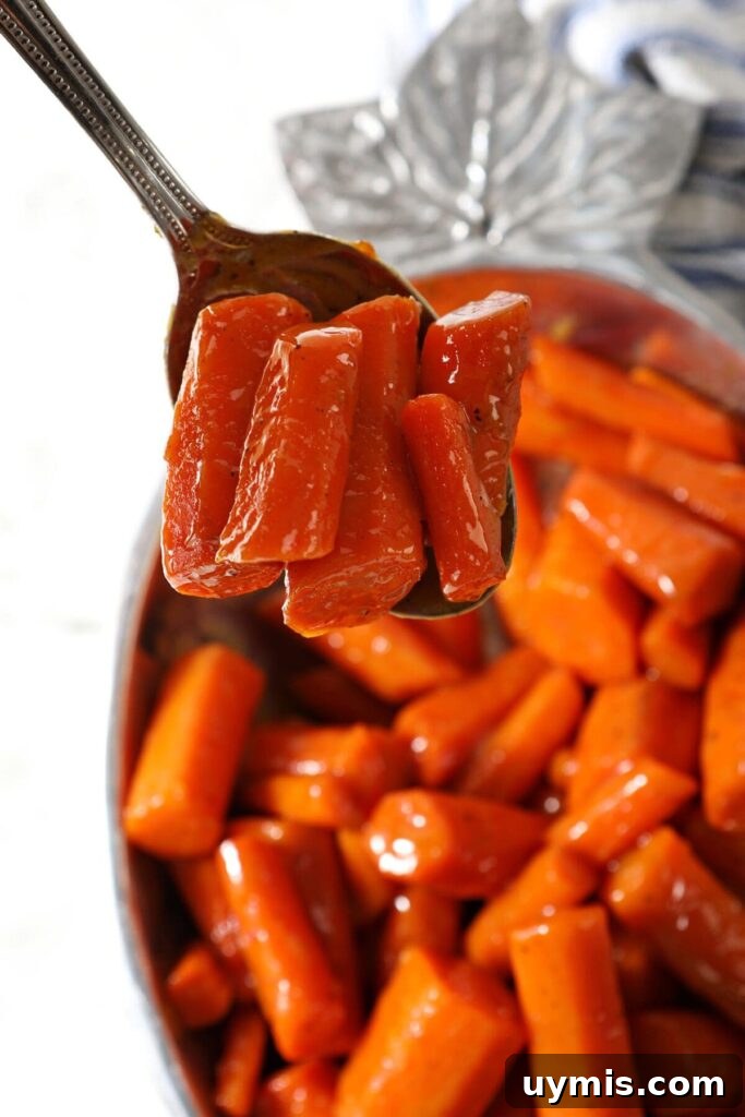 A spoon holds a serving of carrots over a bowl of brown sugar glazed carrots