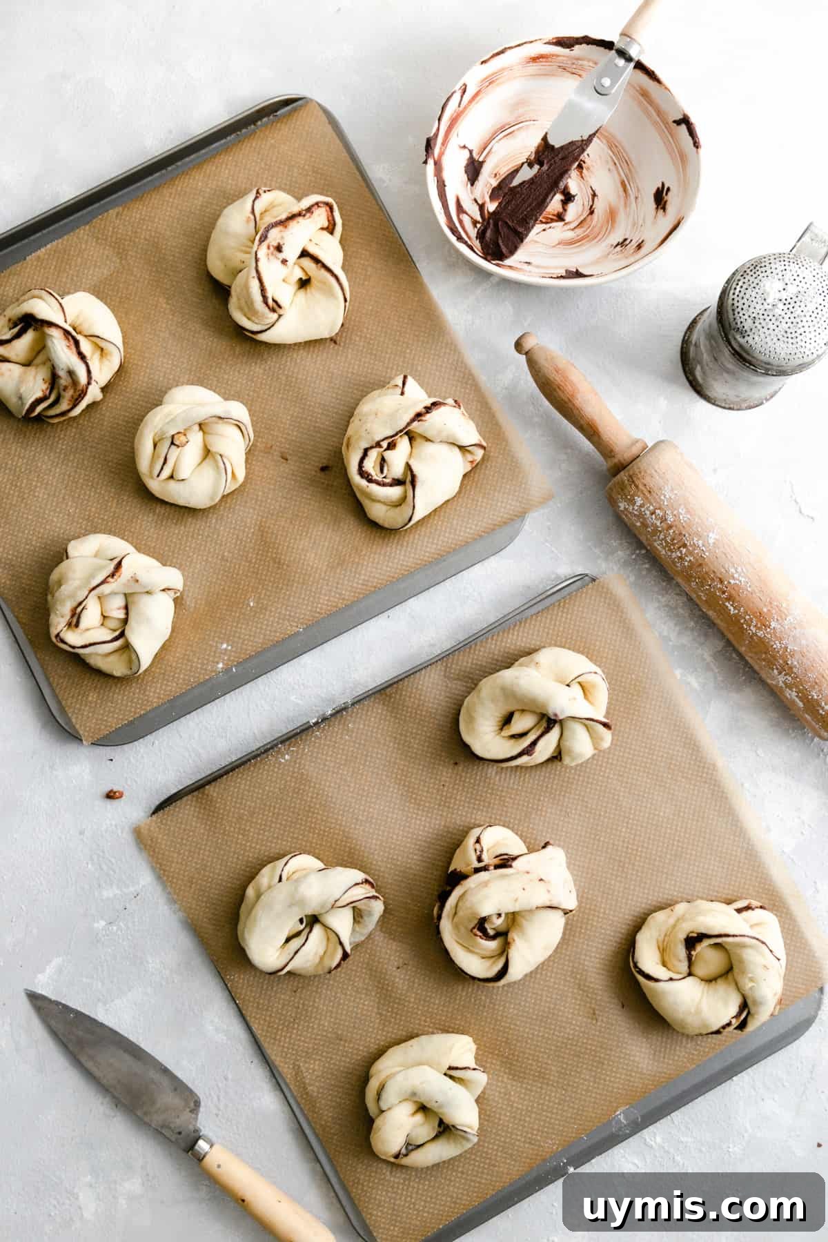 Overhead shot of two baking sheets with unbaked chocolate hazelnut babka buns ready for the oven