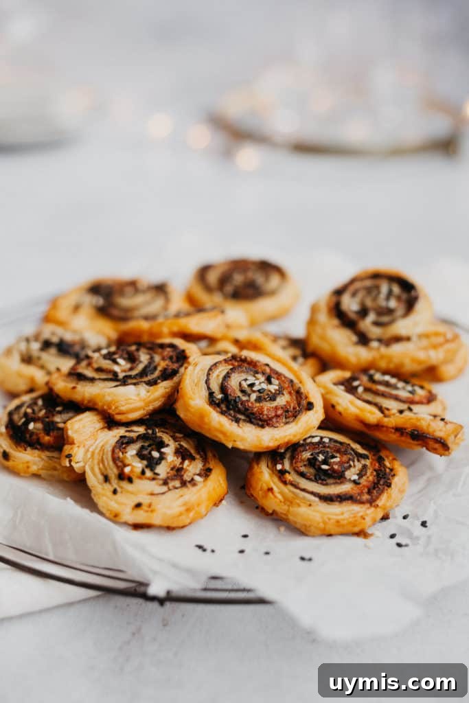 a pile of sesame and tapenade pinwheels on some parchment paper, fairy lights behind