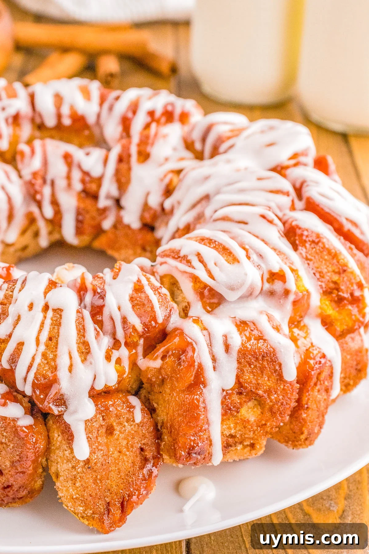 Pull-Apart Cinnamon Roll Monkey Bread Recipe 2 A freshly baked pull-apart bread topped with white icing on a white plate, accompanied by two glasses of milk in the background.