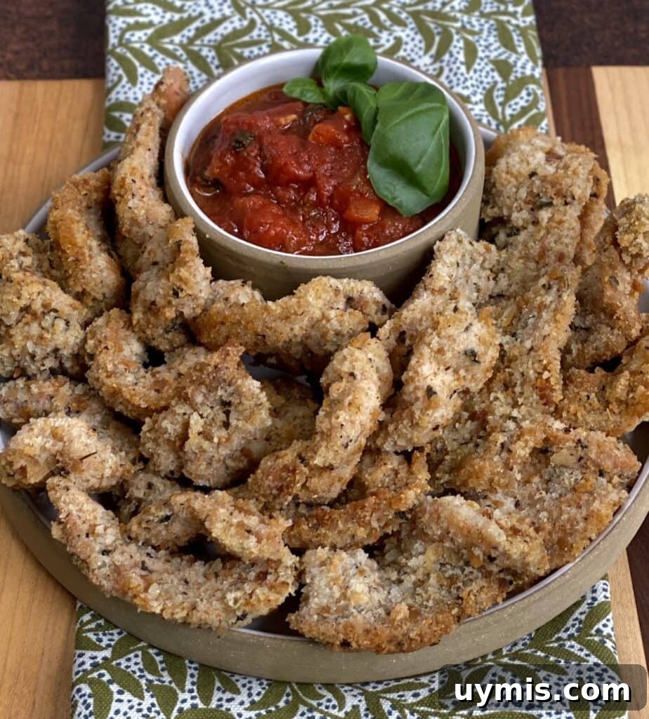 Italian Pan Fried Butterflied Shrimp Recipe 2 Plateful of pan fried butterflied shrimp with small dish of marinara dipping sauce with basil garnish, over a decorative towel.