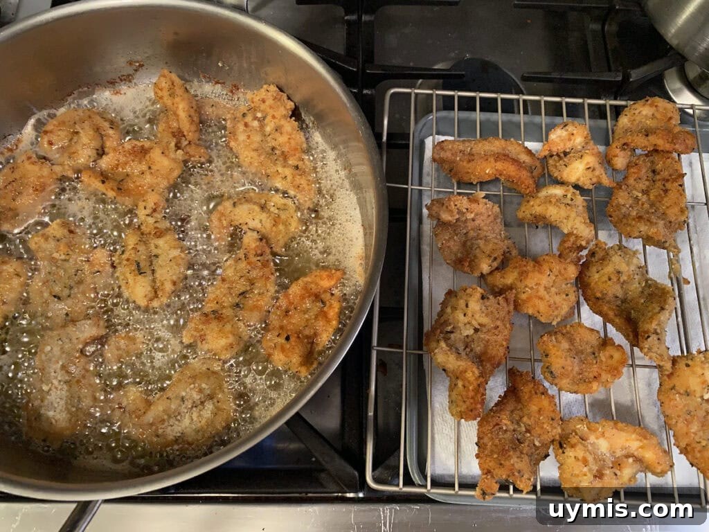 Italian Pan Fried Butterflied Shrimp Recipe 16 Frying the Italian Fried Shrimp in a large stainless steel pan next to some pan fried shrimp draining on a rack over a sheet pan.