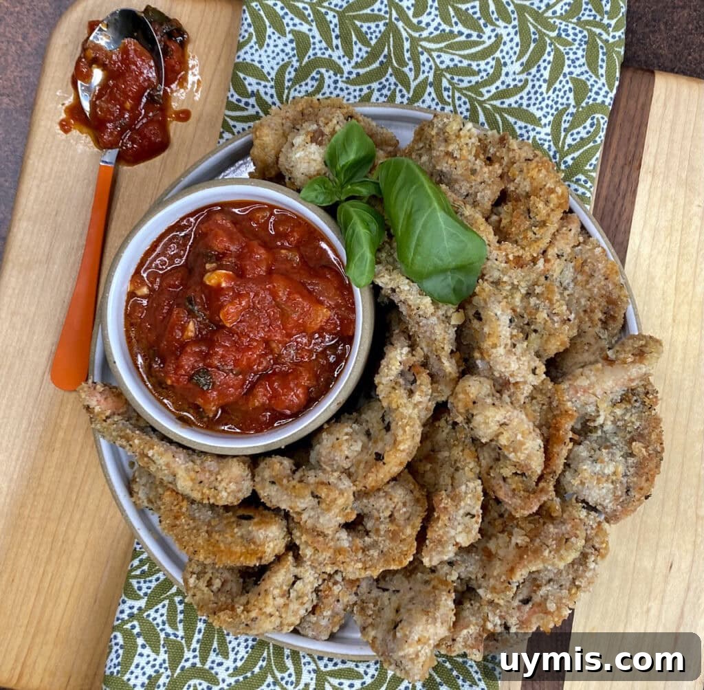 Italian Pan Fried Butterflied Shrimp Recipe 19 Plateful of pan fried butterflied shrimp with small dish of marinara dipping sauce with basil garnish, over a decorative towel with spoonful of tomato sauce in background.