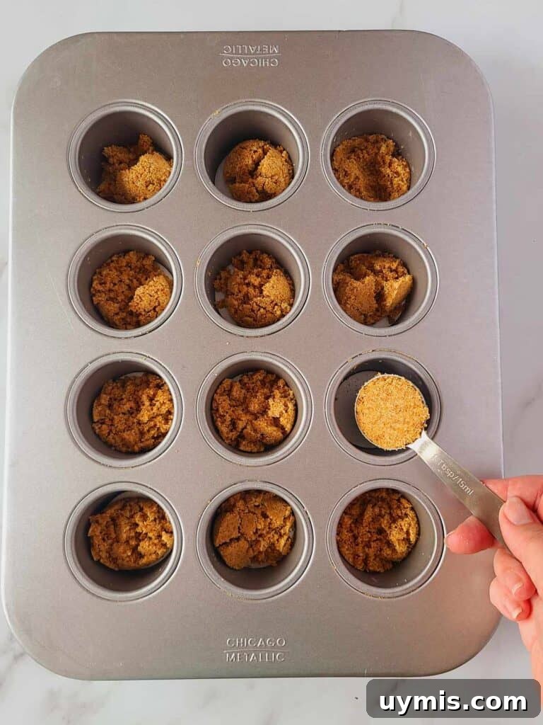 Mini Crème Brûlée Cheesecake Bites Recipe 10 Spooning graham cracker crust into mini cheesecake pan.