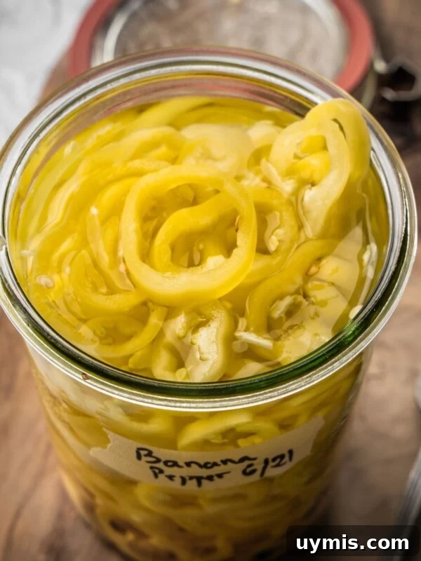 An open jar of pickled banana peppers on a wooden board.