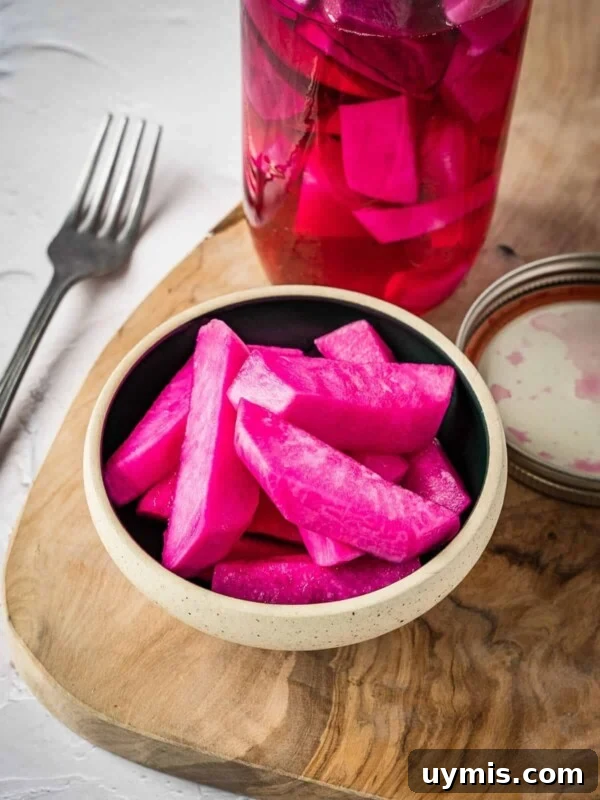 Pink pickled turnips in a bowl on a board.