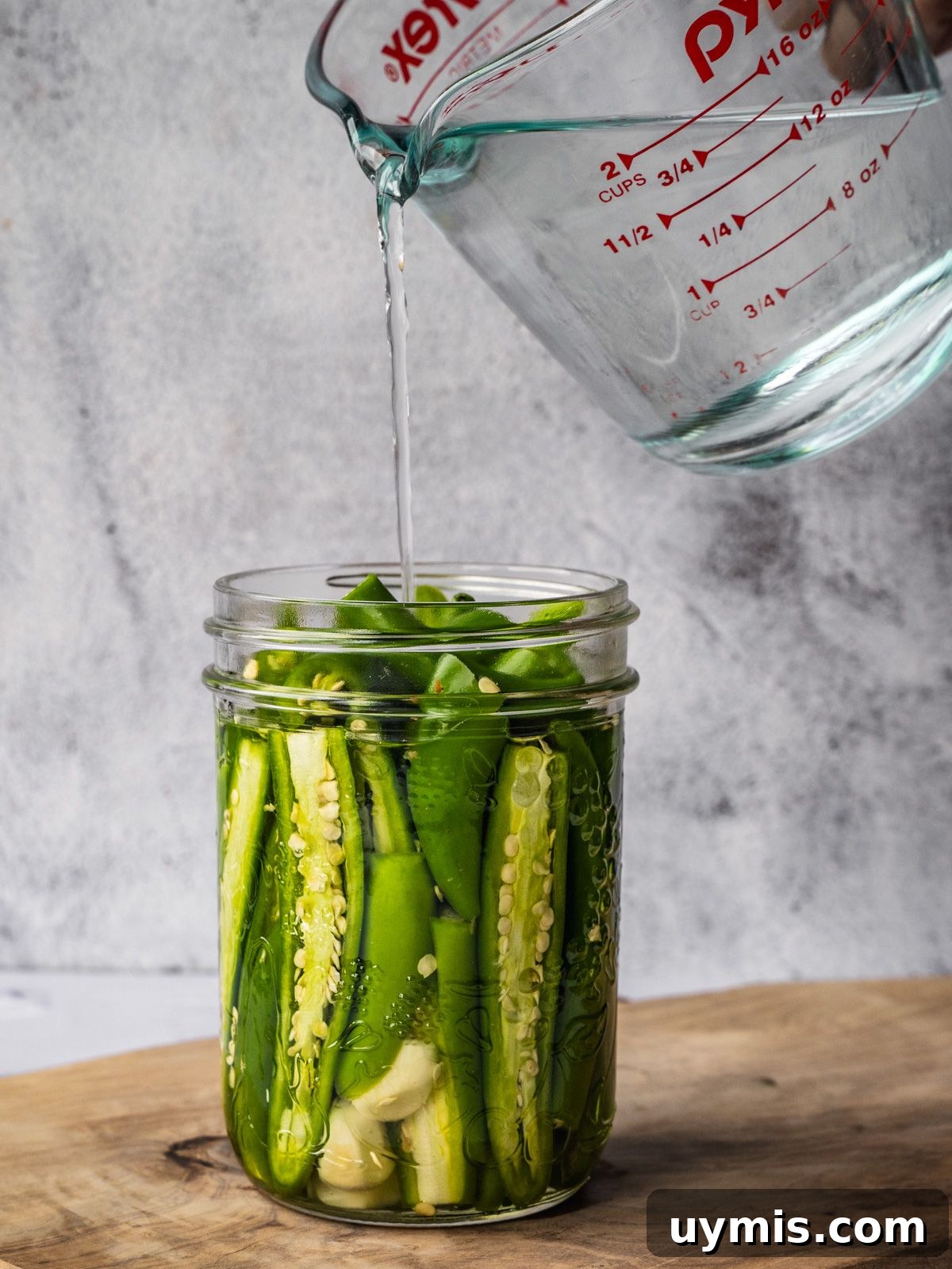 How to Make Pickled Serrano Peppers 6 Pouring pickling solution over peppers and garlic in a mason jar.