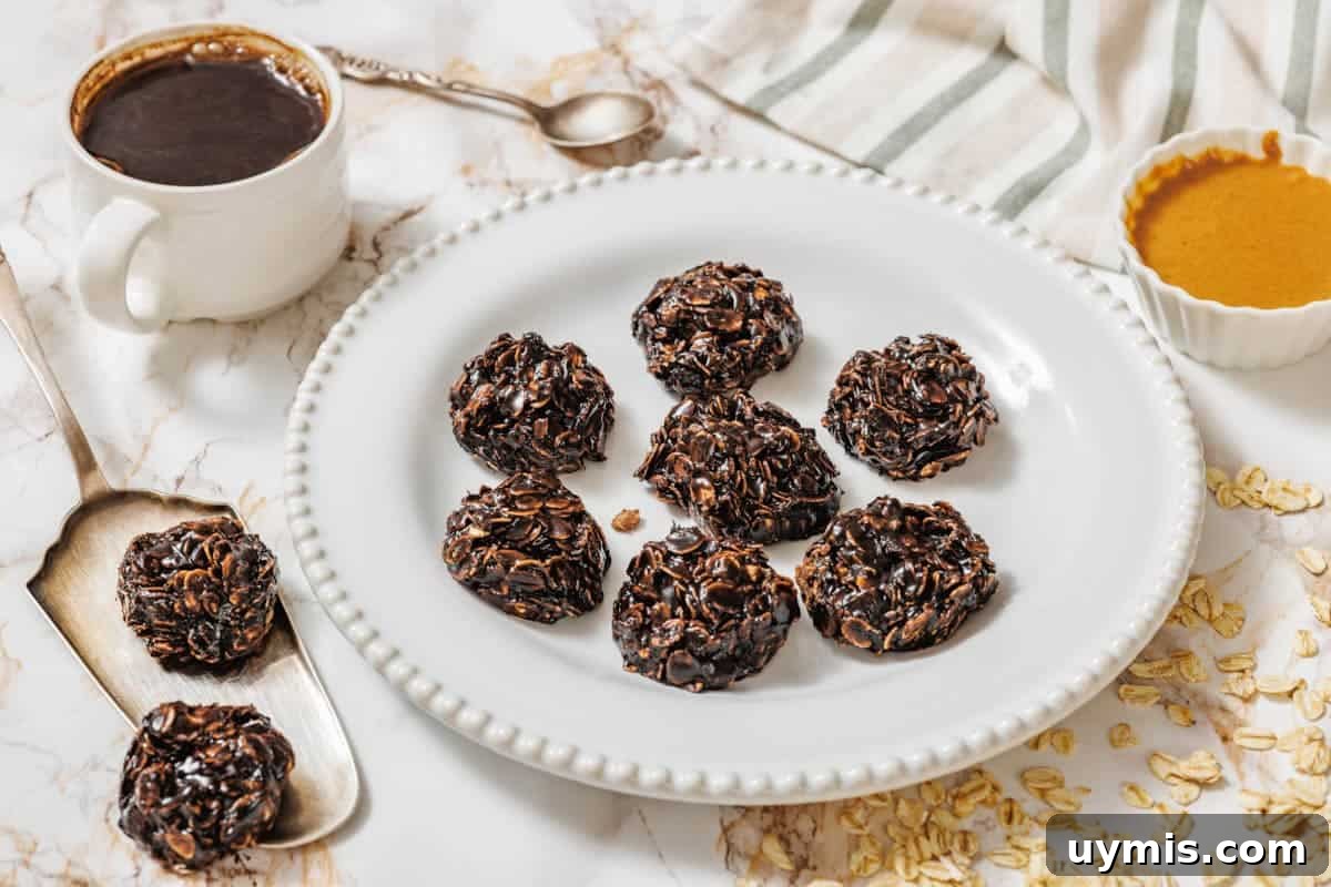 27 Chocolate Desserts You Can't Keep at Home 13 A white plate with seven Peanut Butter No-Bake Cookies on a marble surface, surrounded by a cup of coffee, a spoon, a bowl of nut butter, oats, and a striped cloth.