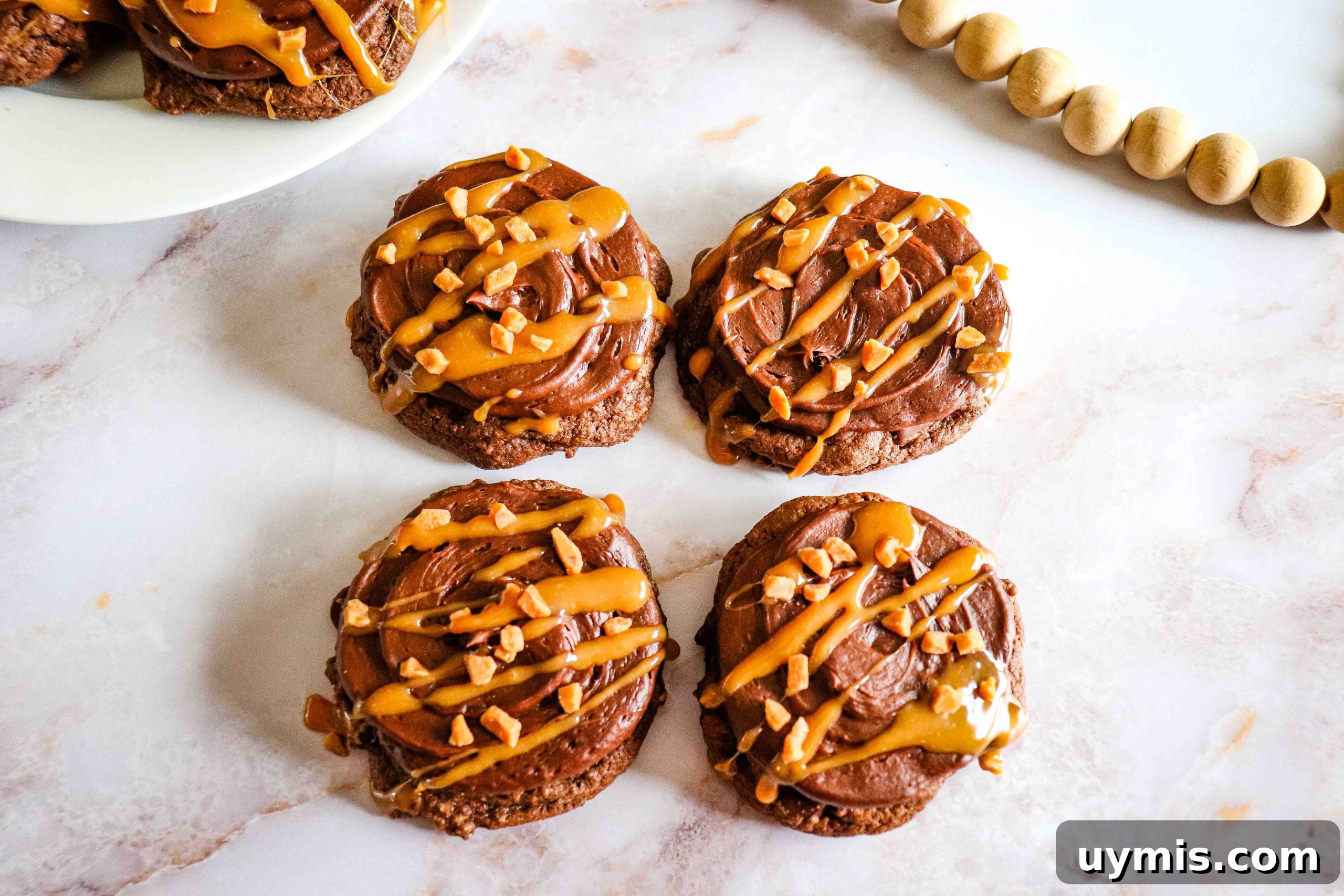 27 Chocolate Desserts You Can't Keep at Home 16 Chocolate Caramel Cookies with frosting, caramel drizzle, and chopped nuts on a white marble surface.
