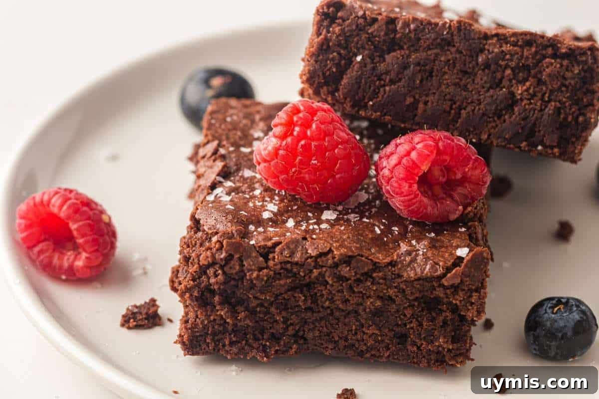 27 Chocolate Desserts You Can't Keep at Home 3 Two Sheet pan chocolate brownies on a white plate, topped with raspberries and a sprinkle of sea salt, with additional raspberries and blueberries on the side.