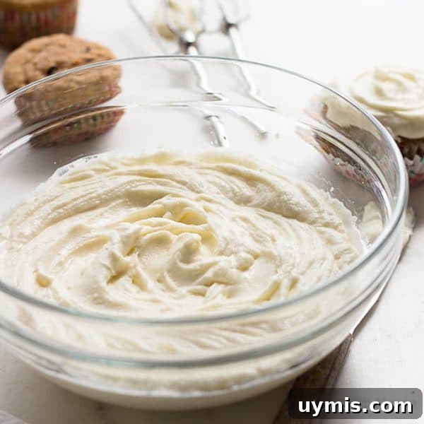 Low-Carb Sugar-Free Cream Cheese Frosting Recipe 5 Bowl of swirled sugar free cream cheese frosting with beaters behind and cupcakes nearby.