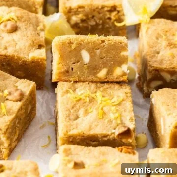 Cut squares of Lemon Blondies sitting on baking paper, with one on an angle to show the texture.