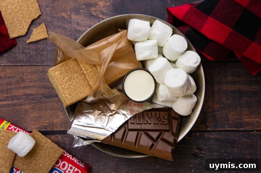 an open chocolate bar, marshmallows, and an open sleeve of graham crackers in a steel pan with a shot glass of cream