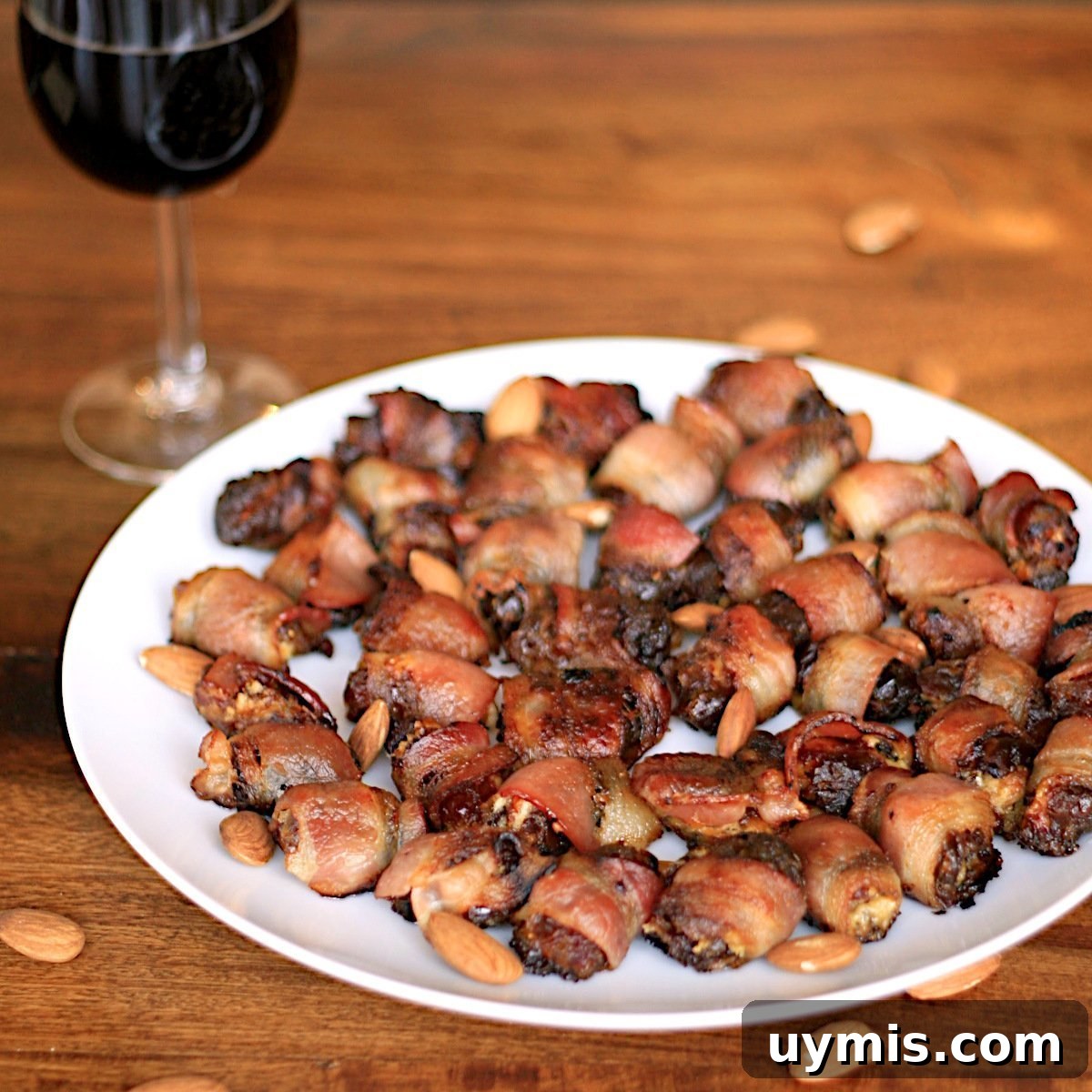Bacon Wrapped Dates Stuffed with Blue Cheese and Almonds 9 Bacon-Wrapped Stuffed Dates on a white plate with a glass of wine.