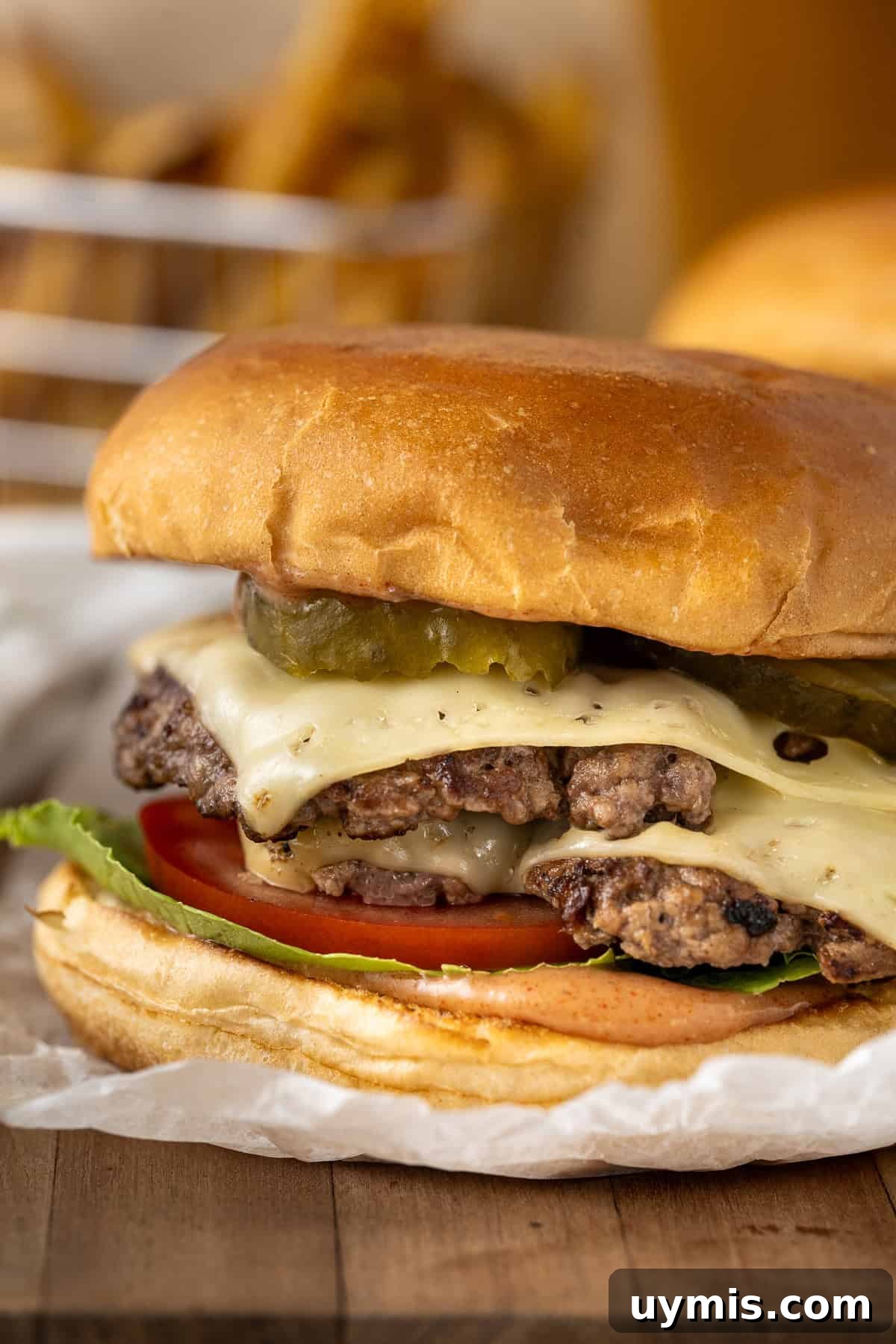 Smash Burger Recipe with Crispy Edges 5 Close up of a double stacked smash burger with cheese and pickles.