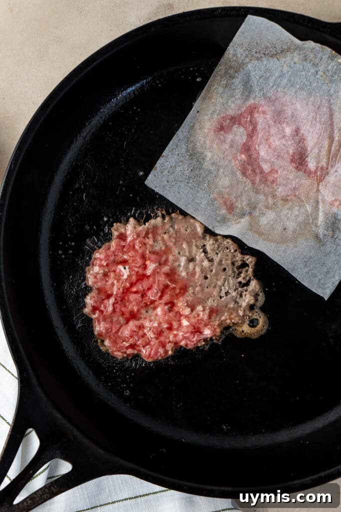Smash Burger Recipe with Crispy Edges 8 Smashing the meat in a cast iron pan.