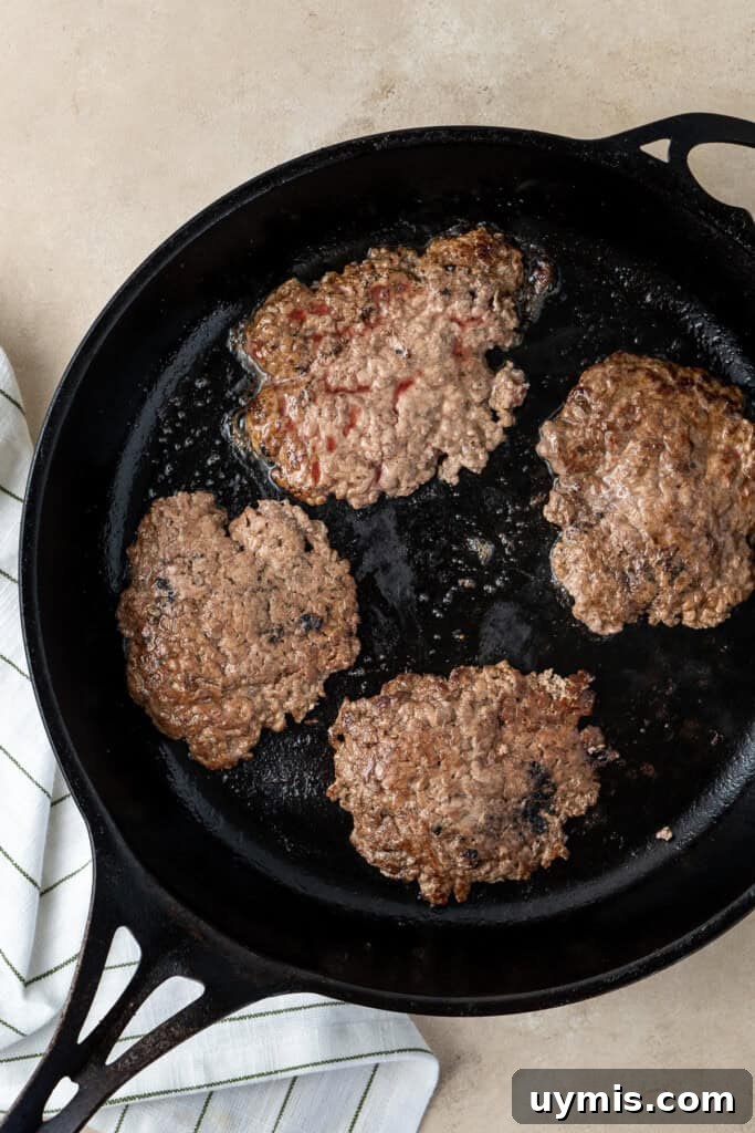 Smash Burger Recipe with Crispy Edges 9 Burger patties cooking in a cast iron pan.