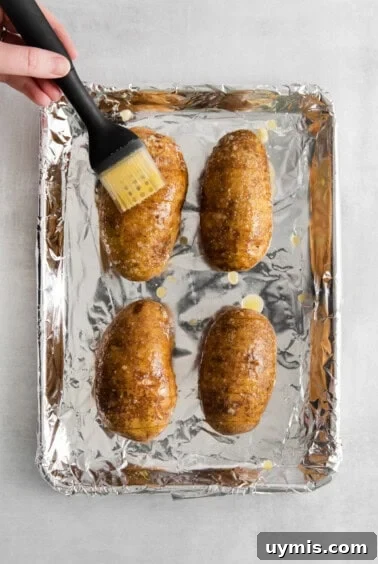 A person brushing potatoes on a baking sheet.