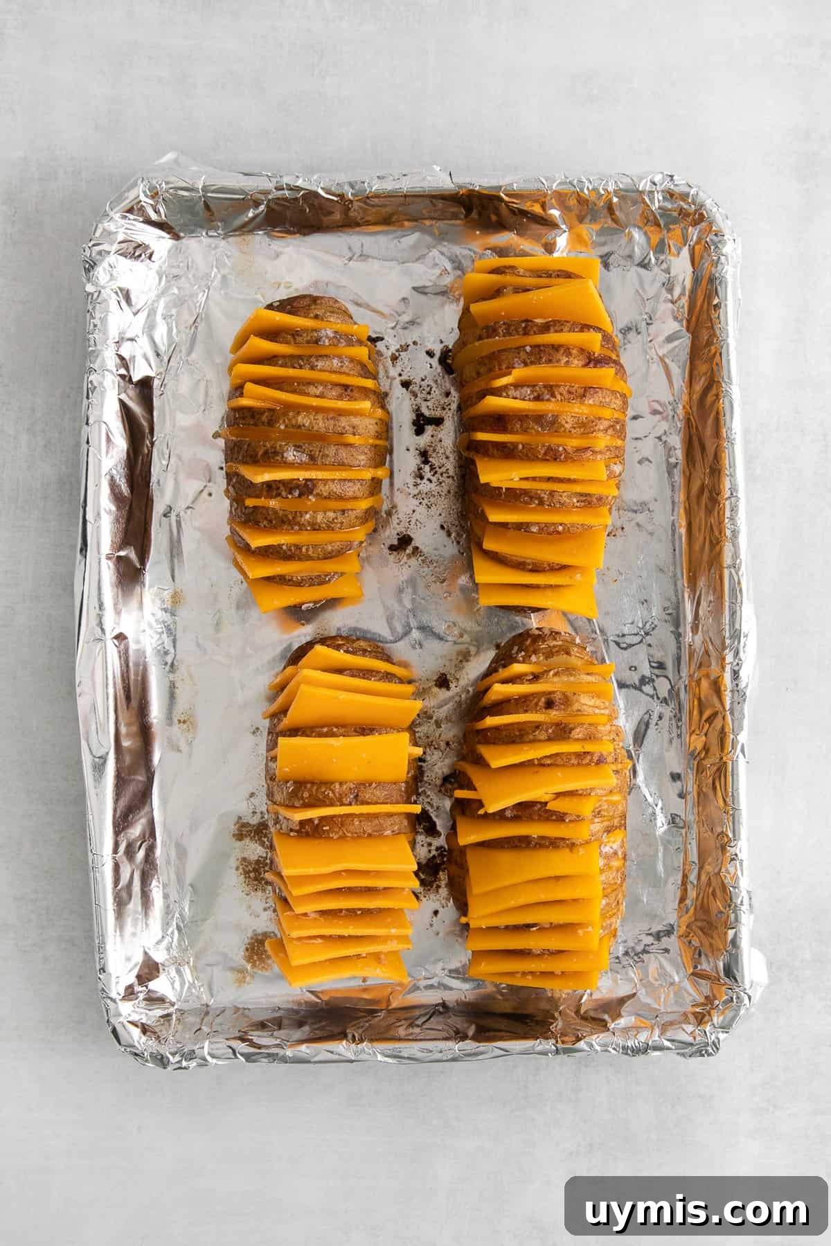 Hasselback potatoes with cheese on a baking sheet.