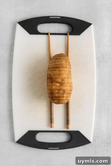 A potato on a cutting board with chopsticks.