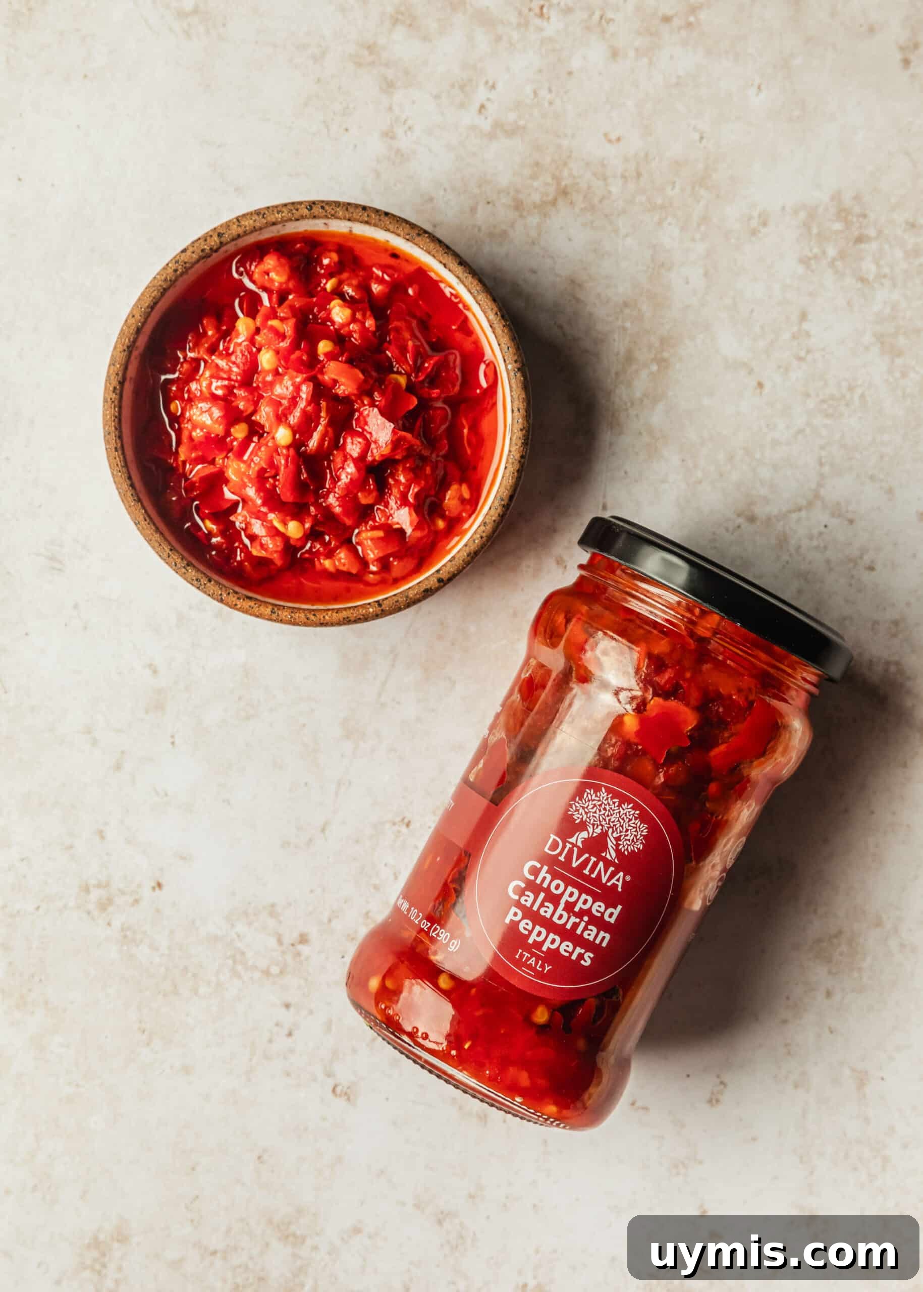 Creamy Spicy Bucatini Carbonara Recipe 4 A brown bowl and jar of Calabrian peppers on a tan counter.