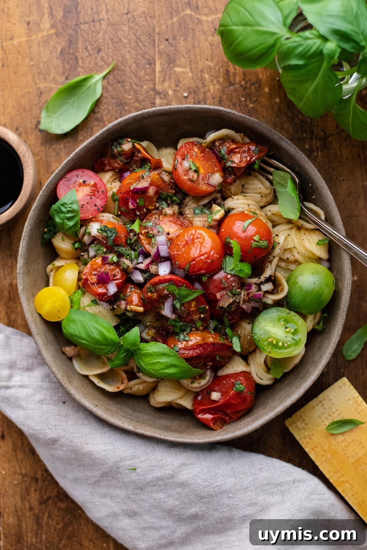 Bruschetta Pasta with Roasted Tomatoes and Basil 2 ceramic dish with bruschetta pasta with tomatoes on wooden background with gray napkin and fresh herbs arranged around it.