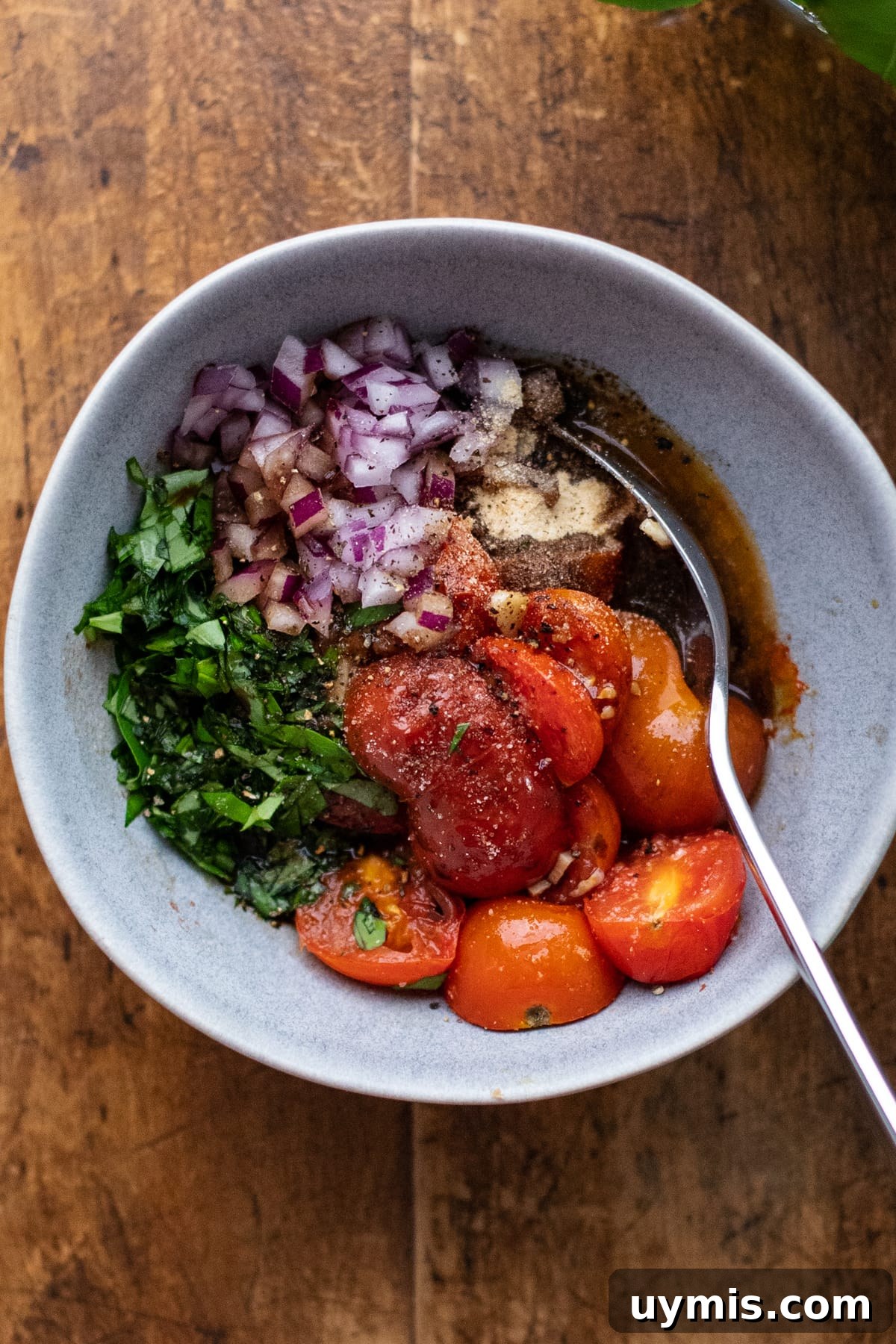 Bruschetta Pasta with Roasted Tomatoes and Basil 6 gray bowl with chopped herbs, red onion, and roasted tomatoes with a wooden background.