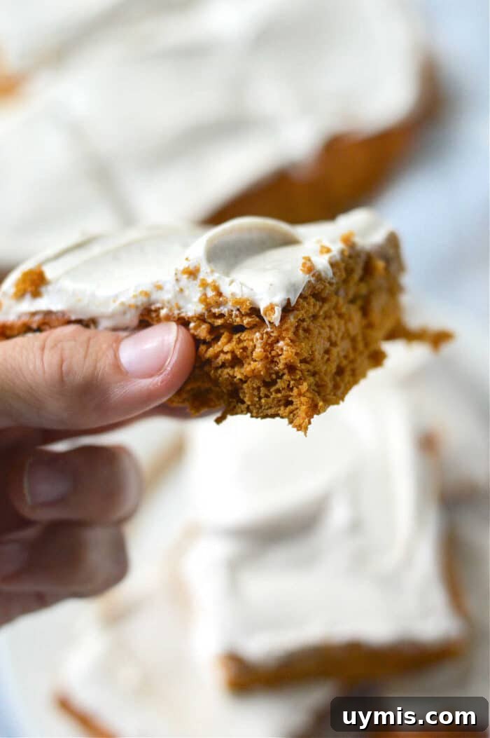 Moist Pumpkin Bars Recipe Made with Cake Mix 2 Close-up of a hand holding pumpkin bars made with cake mix, and more cake pieces in the background.