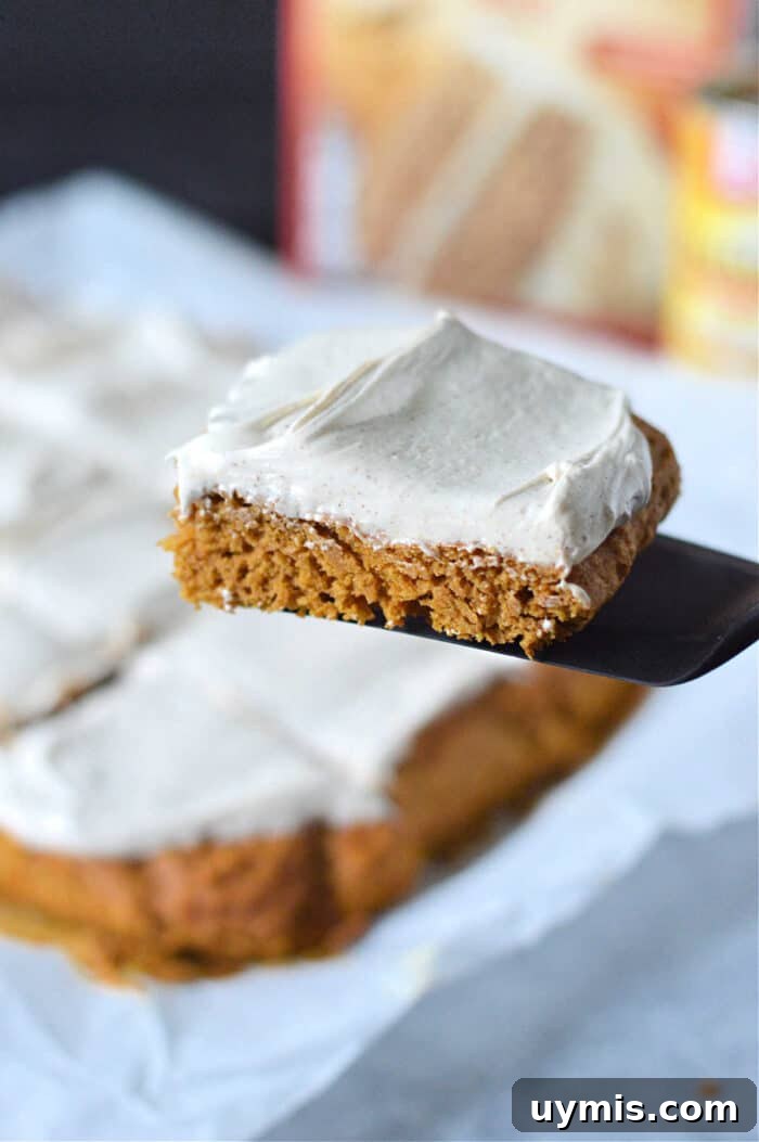 Moist Pumpkin Bars Recipe Made with Cake Mix 6 A frosted square pumpkin bars with cake mix, is lifted on a spatula above more slices on parchment paper.