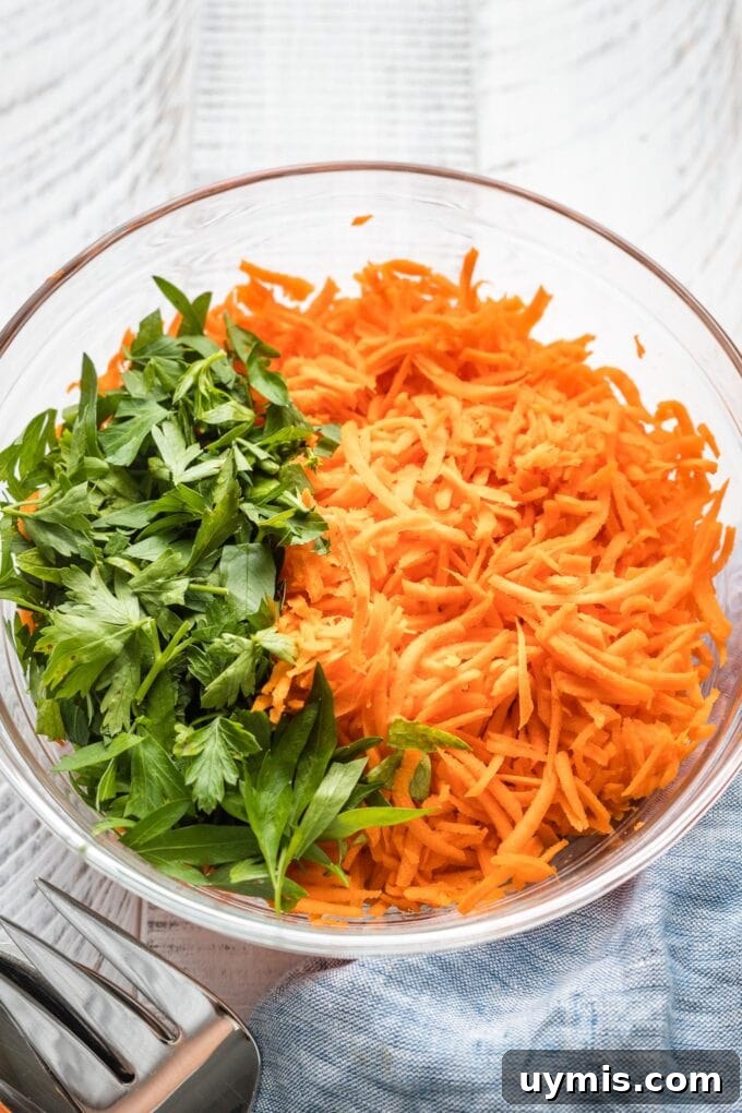 Close up of shredded carrots and chopped parsley in a clear prep bowl.