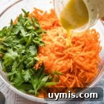 Salad dressing being poured onto a grated carrot salad.