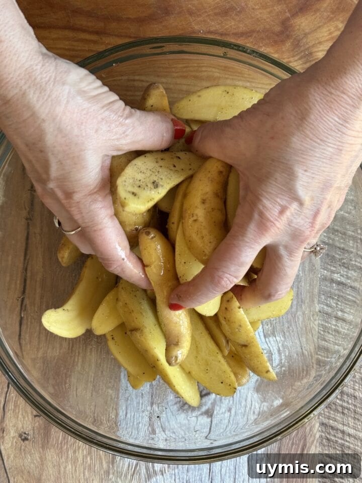 Sheet Pan Sausage and Potatoes Recipe 4 hands tossing fingerling potatoes in olive oil in a glass bowl
