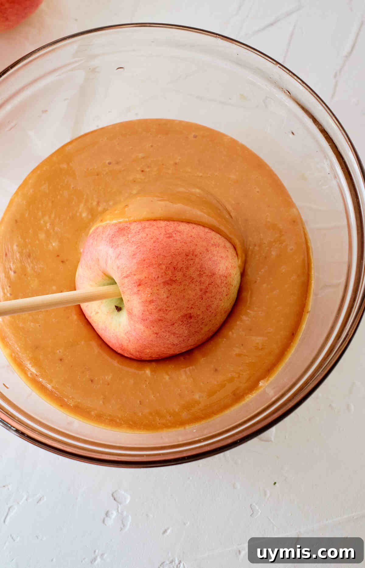 How to Make Caramel Apples: Classic Fall Recipe 4 An apple on a stick being dipped into caramel showing how to make caramel apples.