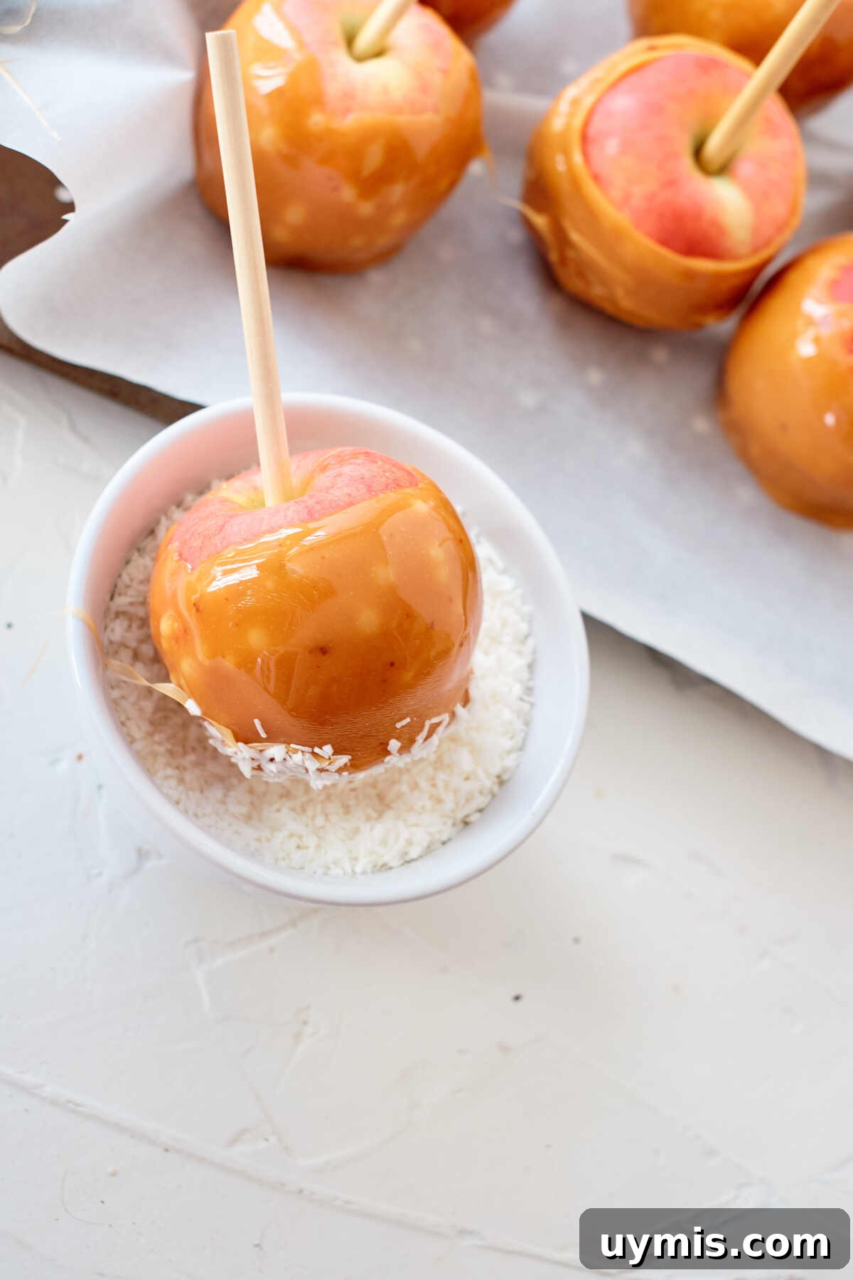 How to Make Caramel Apples: Classic Fall Recipe 5 An apple being dipped into coconut.