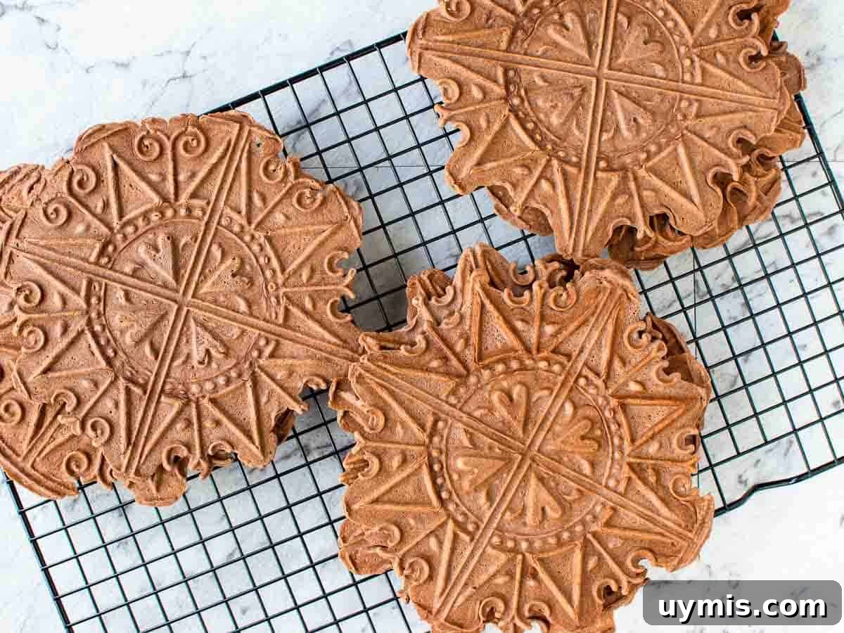 Chocolate Pizzelle Recipe 5 chocolate patterned cookies on a black wire rack.