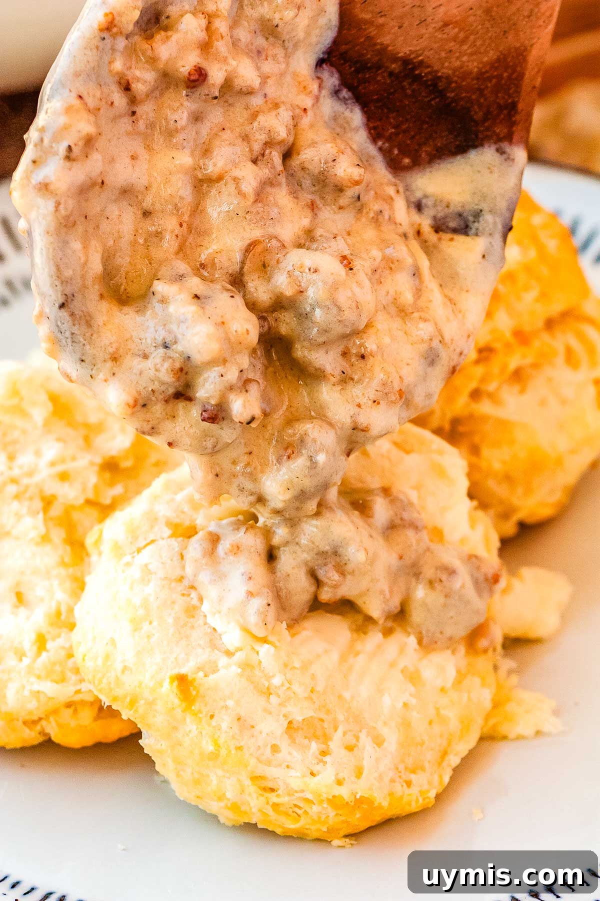 Sausage gravy being spooned over split open biscuits. 